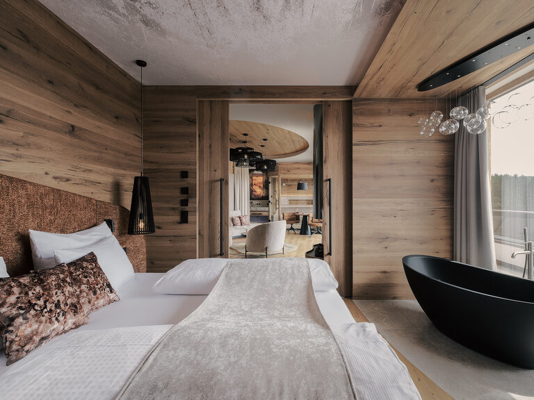 Ein einladendes Schlafzimmer in der Suite des Musikhotels Tonihof mit einem komfortablen Bett und Badewanne und einem großen Fenster, das einen wunderbaren Ausblick eröffnet.